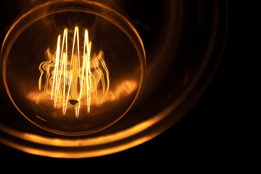 Glowing light bulb on dark background. Close up the filament in a glass bulb.