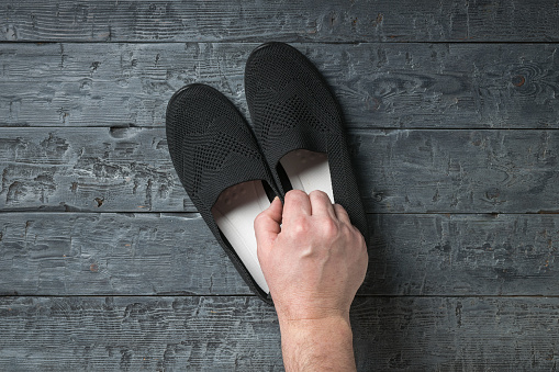 A man's hand with a pair of women's shoes on a wooden background. Casual shoes.