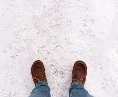 Feet in boots on asphalt covered with snow.