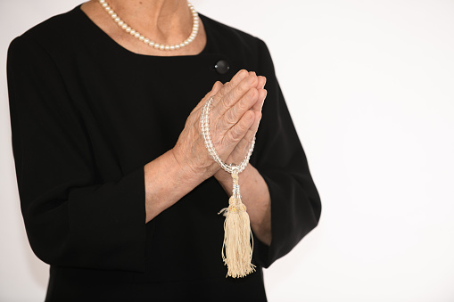 An elderly woman in mourning clothes clasping her hands together