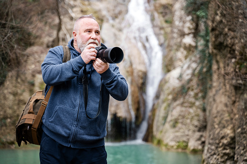 Senior photographer taking photos of a waterfall in the mountains