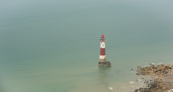 Beachy head lighthouse at the edge of white chalk cliff. Safety warning in the ocean.