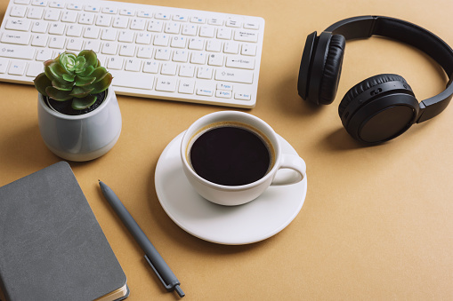 Desktop with coffee cup, notepad, keyboard, succulent plant and headphones on beige table. Top view.