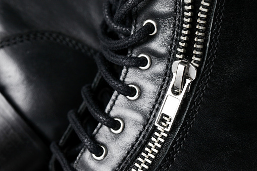 Shoe lacing of the beige waterproofed leather combat boots with ring eyelets, side view of fragment on a white background close-up in selective focus