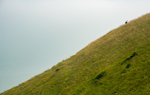 People hiking at the edge of a green cliff along the ocean at mist. People active outdoors. Healthy life style. Beachy head United Kingdom