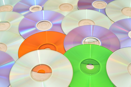 Pile of multicolored CDs and DVDs on the brown wooden table. Vintage technology concept. Selective focus.