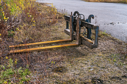 Tractor fork attachment stored on gravel ground at a side of asphalt road