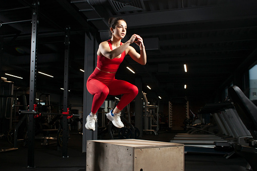 young athletic girl in red sportswear jumping in a black gym, attractive woman doing sports in the fitness room