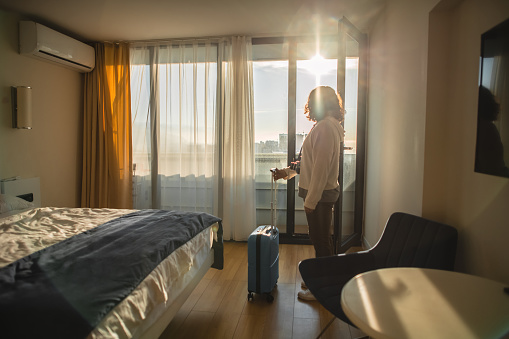 Woman with suitcase arrives at a hotel room for summer holiday. Travel and tourism concept.