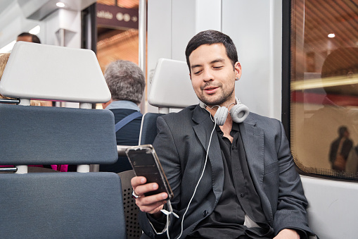 latino man sitting on train using his smart phone while travelling on public transport