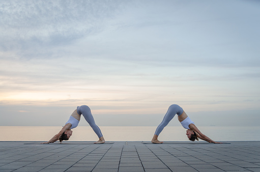 Girls practicing yoga outdoors. Sea in the background of the image. Tranquility and relaxation.