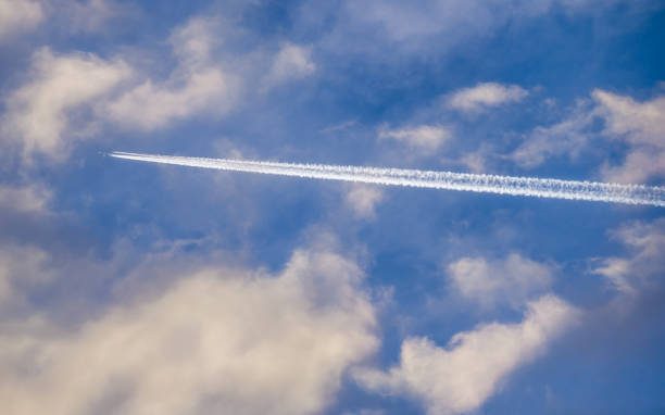 istock White trail of plane flying among white clouds in blue sky 2017513222