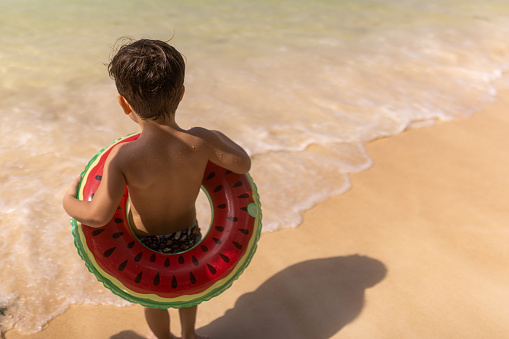 Cute little boy walking in the sea with swim ring, he is on vacation in Thailand.