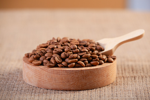 Roasted coffee grains with wooden scoop on jute burlap.
