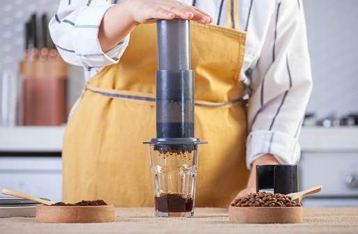 Woman brews coffee by pressing Aeropress in the kitchen