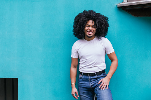 Happy Afro-Latino man with a bright smile stands confidently against a vivid turquoise background, exuding casual charm.