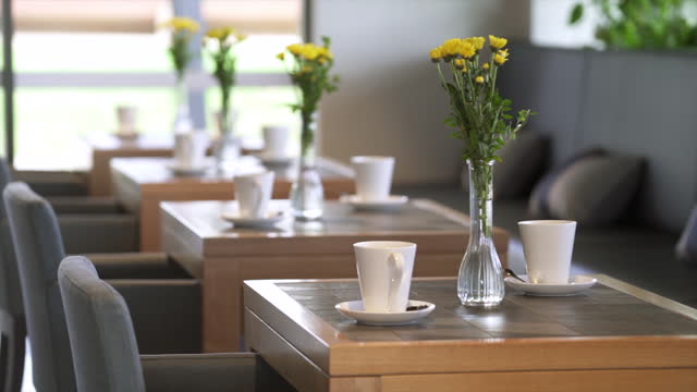 A vase of fresh flowers and coffee cups on dining tables in an modern and stylish cafe and restaurant