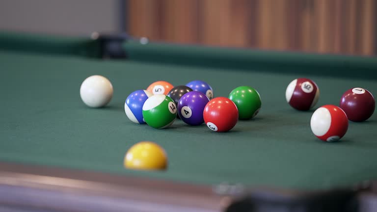 Pool balls scatter on a dark green felt pool table after a break, a popular social game in pubs