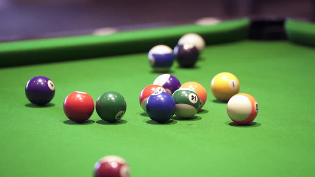 Pool balls scatter on a green felt pool table after a break, a popular social game in pubs