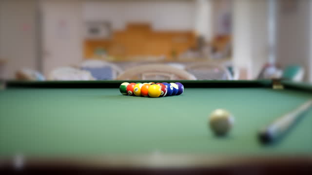 Stylized selective focus shot of pool balls lined up on a pool table ready for a game, with the camera slowly elevating and tilting down onto the balls.