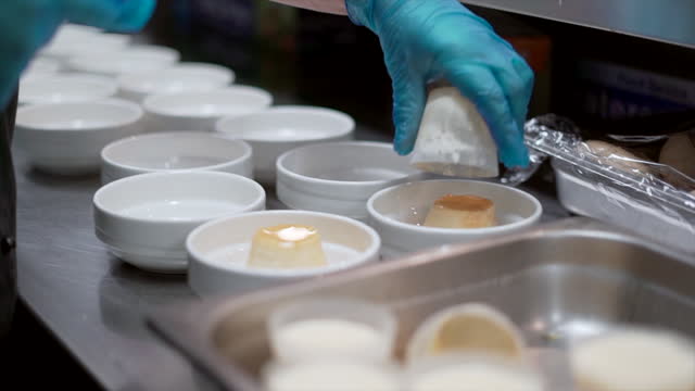 Bowls lined up in a commercial kitchen with a chef preparing panna cotta ready for service in a hotel restaurant