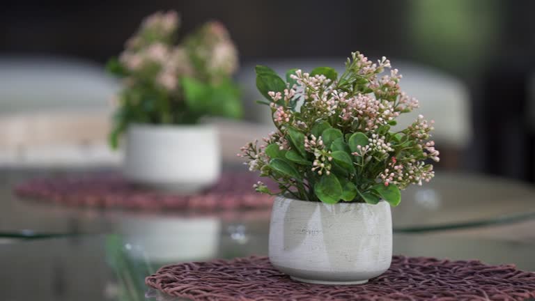 A small old fashioned bouquet of flowers in a ceramic vase on a glass dining table.