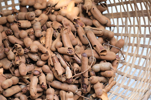 A fresh pile of ripe sweet tamarind is dried in the sun in a bamboo basket on an Asian fair in Thailand. A close-up of the tamarind in the basket.