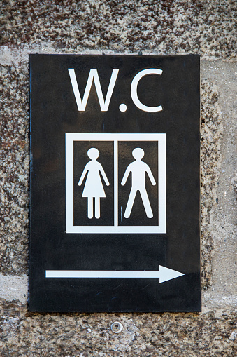 Rectangular sign on a black background on a granite wall with directional arrow pointing to toilets