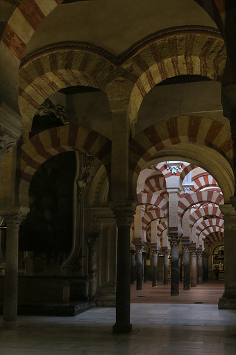 close up of a portion of the interior of the Mosque-Cathedral of Cordoba, known both as the Cathedral of the Cordoba Diocese and, also, the Great Mosque of  Cordoba, featuring decorative, striped, arches