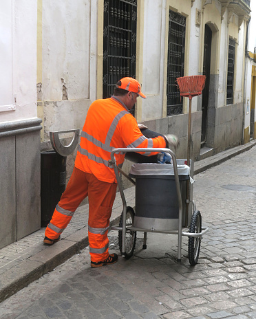 municipal worker, dressed in orange for safety, in Cordoba, Spain, sweeping the streets and collecting roadside trash in the historic downtown district