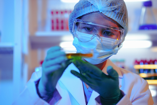 Asian female scientist passionately conducts experiments in a laboratory, surrounded by petri dishes and beakers. Delve into the chemistry of gasoline, food ingredients, and perfumes