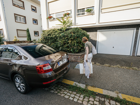 Paris, France - Sep 8, 2018: Young woman near car trunk with multiple bags after shopping near her garage door Skoda Octavia Car