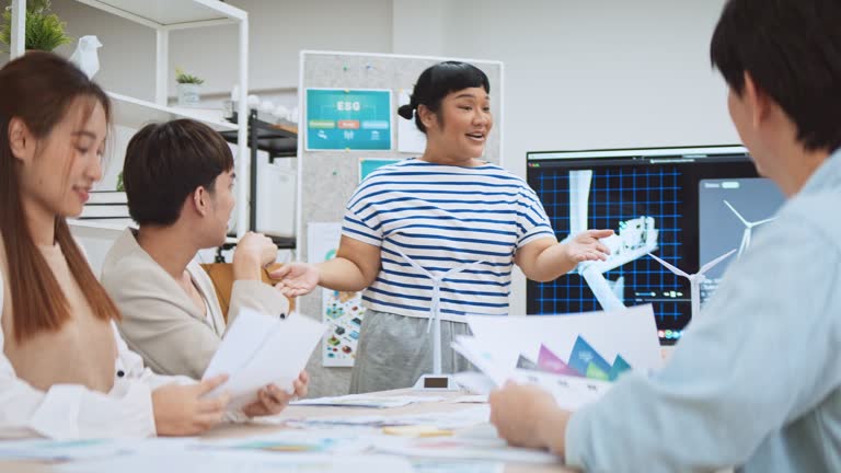 Asian business people team brainstorm meeting in sustainable corporate office. Presentation ESG project planning, solar panel, wind turbine power energy generation. Environmental conservation concept