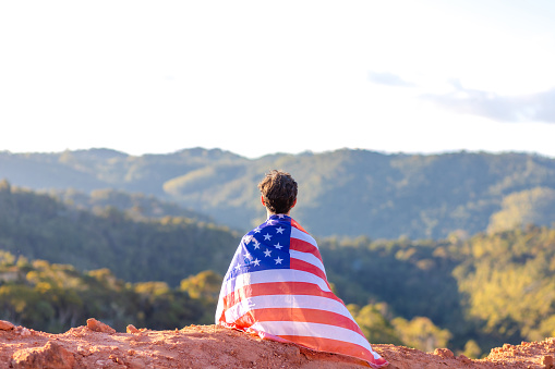 American seated atop a mountain, draped in the American flag, surrounded by a mountainous landscape. Ideal for campaigns celebrating American pride and showcasing the United States' support for athletes in major sporting events