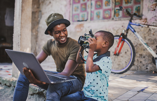 young african dad using laptop and camera with his children