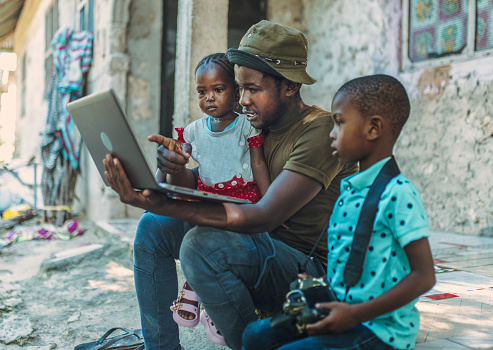 young african dad using laptop and camera with his children