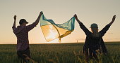 Energetic Ukrainian couple raising the flag of Ukraine over a field of wheat at sunset