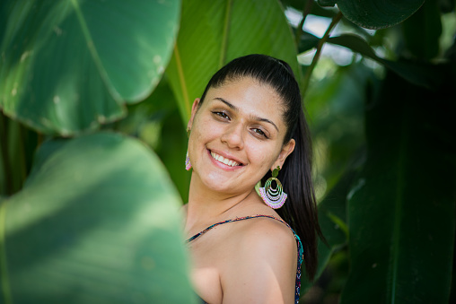 close-up of a short-haired latina woman smiling and looking at the camera in the middle of the forest.