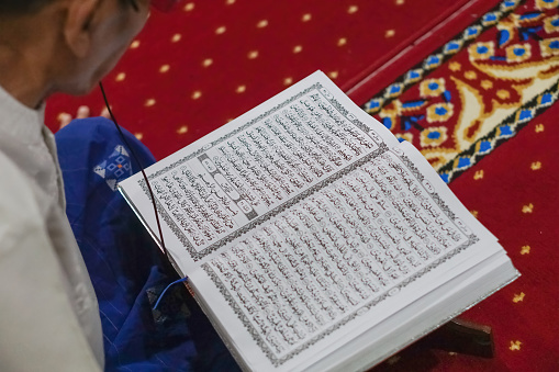 Jakarta, Indonesia - April 12, 2023: Close up photo of a Muslim man reading the Holy Quran. Selective focus.