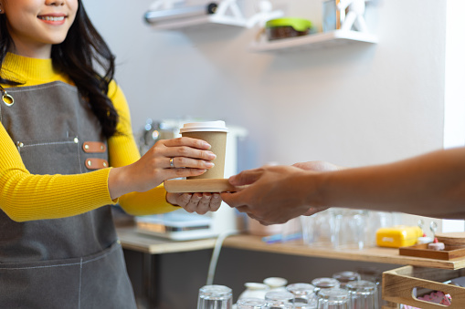 Young barista or waitress holds a coffee cup and serves it to a customer.