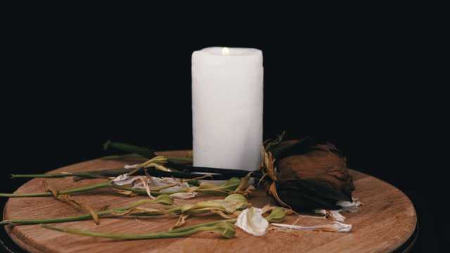 Burning White Candle and Two Withered Dry Roses Rotate on a Black Background