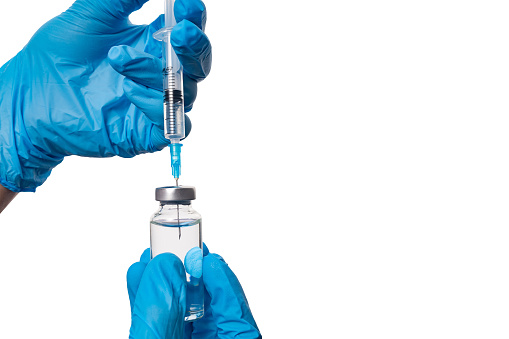 Gloved hands drawing liquid from a vial into a syringe, isolated on a white background.