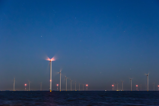 Off shore wind turbines or wind mills at sea at blue dusk or night , long exposure and stars visible. High quality photo