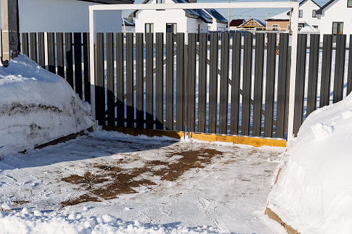 The adjoining territory, the entrance to the house is cleared of snow, the gate is made of corrugated sheeting, the fence is picket. Winter in the yard. High quality photo