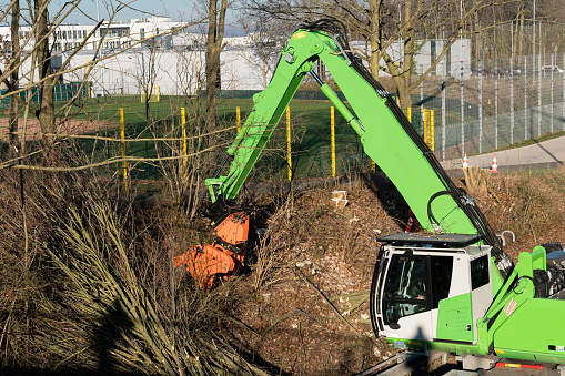 A green excavator clearing bushes along the city road.