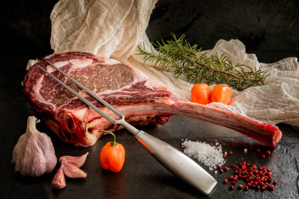 Wagyu tomahawk steak on a slate background with salt, pepper, garlic and peppers