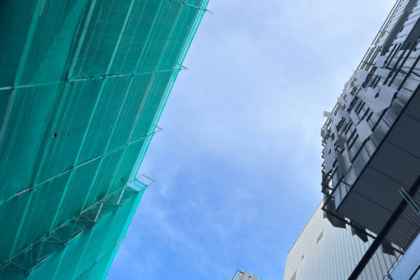 Bottom view of nearby buildings with scaffolding and protective green mesh.