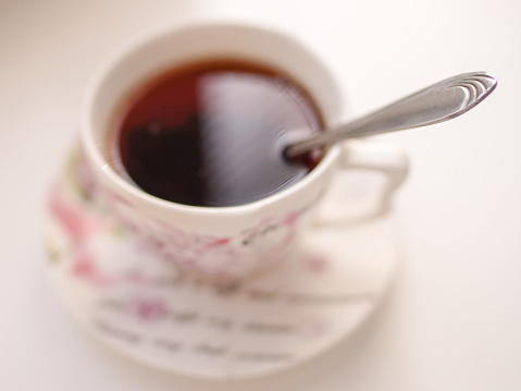 Spoon in a cup of drink. Cup of tea on a saucer in blur on a white table