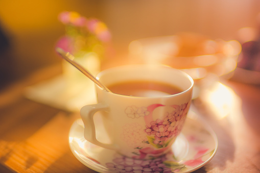 Cup of tea on a saucer with spoon. Warm light in room. Cozy atmosphere