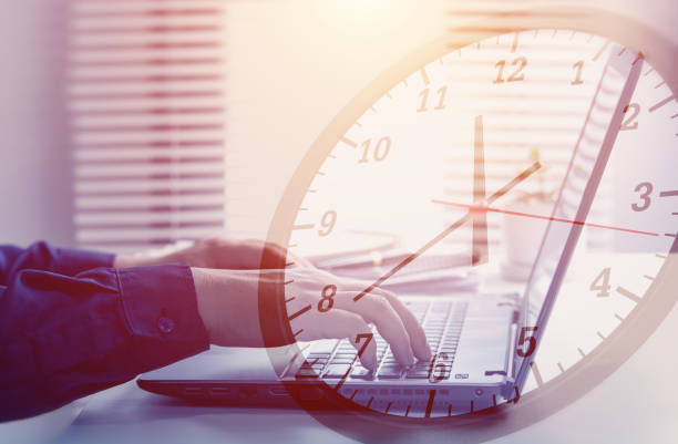 istock Working hours and working overtime. Close-up view of an employee typing on computer with clock overlapping. 2017992994